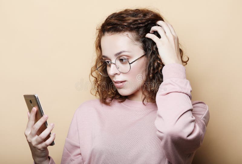 Concetto emozionale e della gente di stile di vita: Giovane bella donna riccia con lo smartphone immagine stock Concetto emozionale e della gente di stile di vita: Giovane bella donna riccia con lo smartphone immagine stock