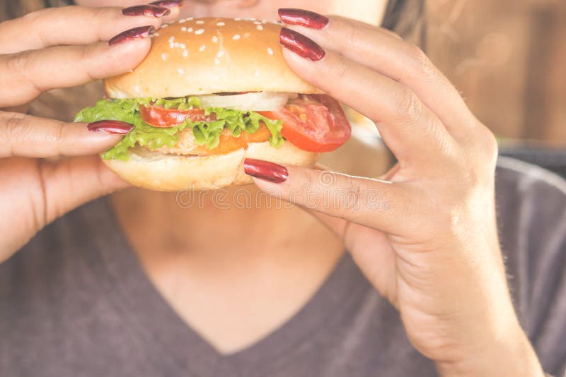 Concetto non sano degli alimenti industriali del primo piano dell'hamburger di cibo della mano della donna fotografia stock libera da diritti Concetto non sano degli alimenti industriali del primo piano dell'hamburger di cibo della mano della donna fotografia stock libera da diritti