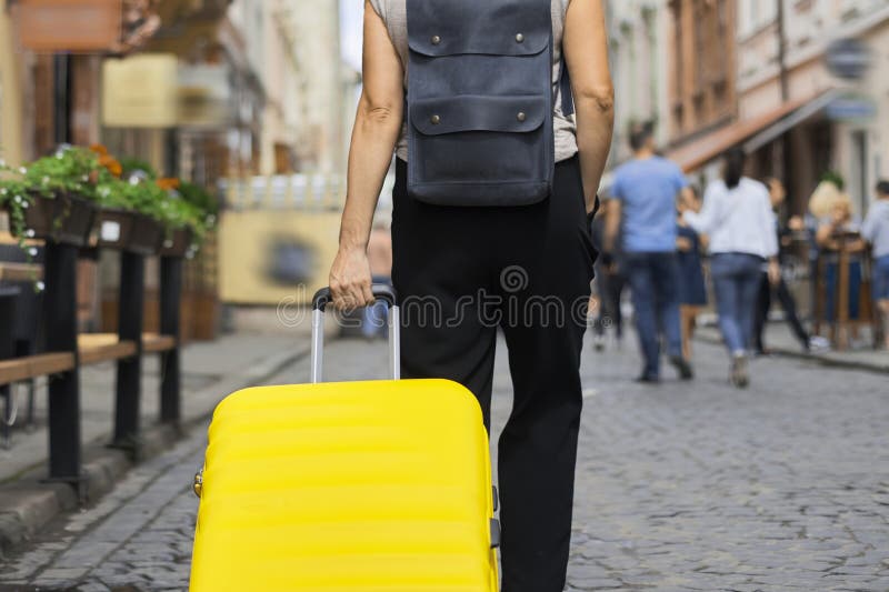 Concetto turistico di trasporto bagagli, chiusura di valigia gialla in mano a una donna che cammina