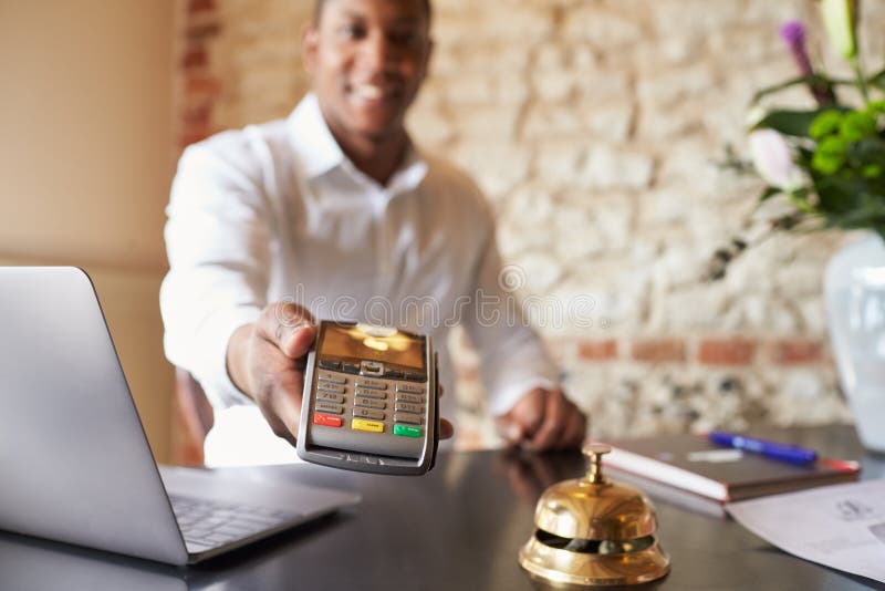 Concierge at hotel reception holds credit card reader to camera stock image