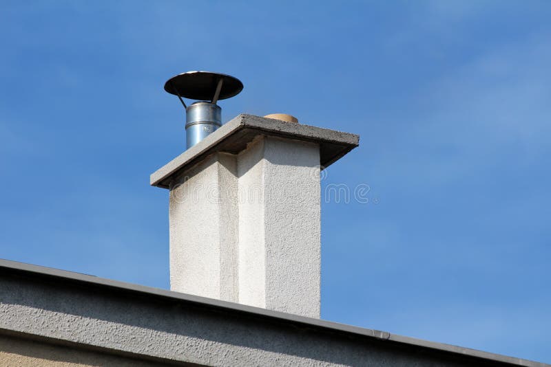 Concrete white chimney with shiny metal top and protective cap on top of old suburban family house