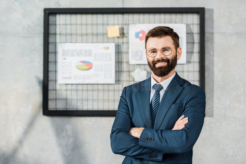 condizione barbuta sicura bella dell'uomo d'affari con le armi attraversate e sorridere alla macchina fotografica immagini stock libere da diritti condizione barbuta sicura bella dell'uomo d'affari con le armi attraversate e sorridere alla macchina fotografica immagini stock libere da diritti