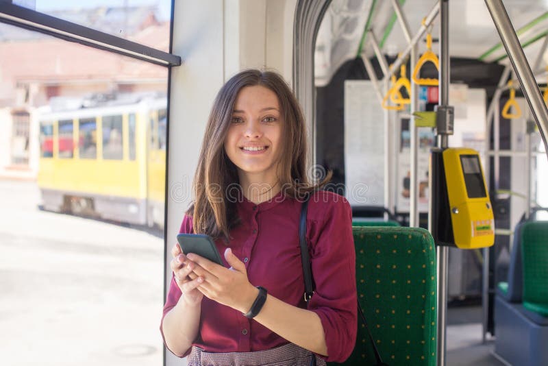 Condizione del passeggero della giovane donna con lo smartphone mentre muovendosi nel tram moderno immagini stock Condizione del passeggero della giovane donna con lo smartphone mentre muovendosi nel tram moderno immagini stock