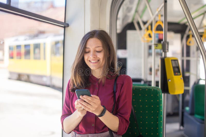 Condizione del passeggero della giovane donna con lo smartphone mentre muovendosi nel tram moderno immagini stock Condizione del passeggero della giovane donna con lo smartphone mentre muovendosi nel tram moderno immagini stock