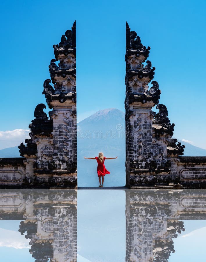 Condizione del viaggiatore della donna ai portoni antichi dei portoni del tempio di Pura Luhur Lempuyang aka di cielo in Bali fotografia stock libera da diritti Condizione del viaggiatore della donna ai portoni antichi dei portoni del tempio di Pura Luhur Lempuyang aka di cielo in Bali fotografia stock libera da diritti