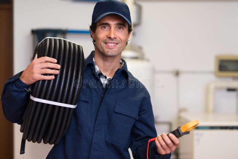 Condotto ondulato di trasporto sorridente del lavoratore e un tester fotografie stock libere da diritti Condotto ondulato di trasporto sorridente del lavoratore e un tester fotografie stock libere da diritti