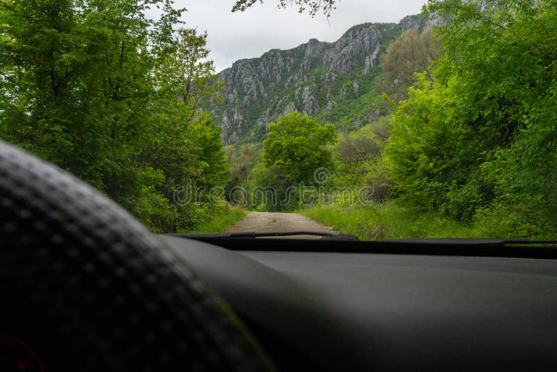 Conduire la voiture dans la montagne dans un chemin avec la forêt verte et les grandes roches Vue de conducteur avec le volant no photographie stock Conduire la voiture dans la montagne dans un chemin avec la forêt verte et les grandes roches Vue de conducteur avec le volant no photographie stock