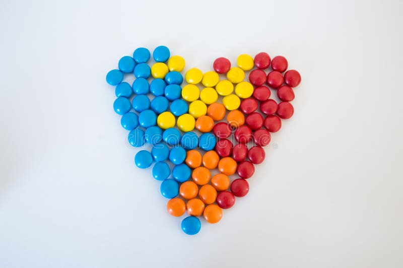 Confetti rotondi multicolori delle caramelle presentati sotto forma di un cuore su un fondo bianco immagini stock Confetti rotondi multicolori delle caramelle presentati sotto forma di un cuore su un fondo bianco immagini stock