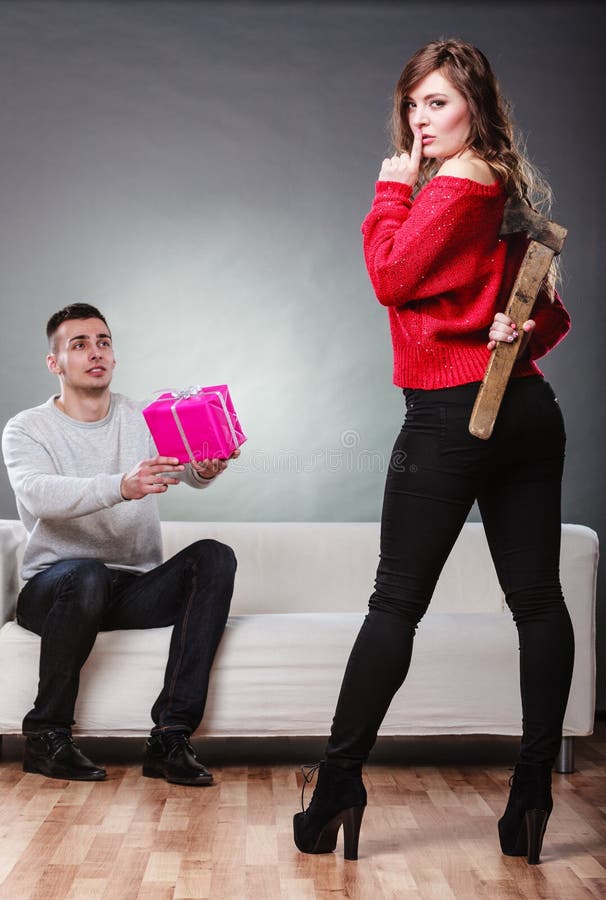 False feelings, relations problem. Trusting guy giving present pink box to misleading girl. Insincere women holding axe behind her back. False feelings, relations problem. Trusting guy giving present pink box to misleading girl. Insincere women holding axe behind her back