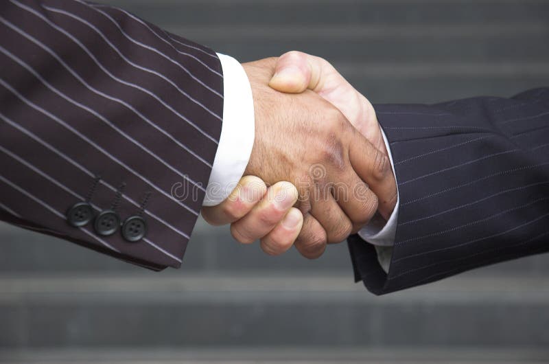 Businessmen in pinstripe suits shake hands in front of office steps. Businessmen in pinstripe suits shake hands in front of office steps.