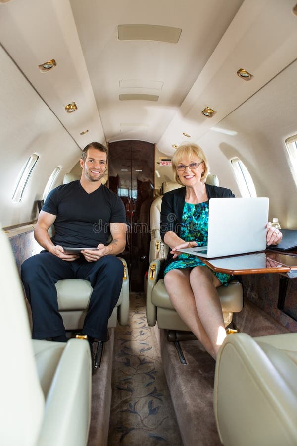 Confident Business People In Corporate Jet. Portrait of confident business people with laptop and digital tablet in corporate jet stock photos Confident Business People In Corporate Jet. Portrait of confident business people with laptop and digital tablet in corporate jet stock photos