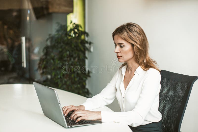 Confident business woman working with computer in office. Sexy blonde female boss using laptop. Successful business