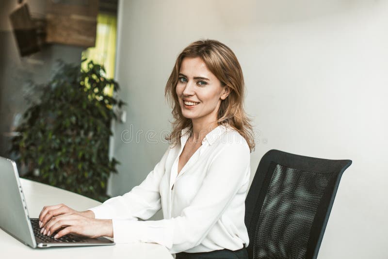 Confident business woman working with computer in office. She is wearing a white blouse and a black skirt. Office worker