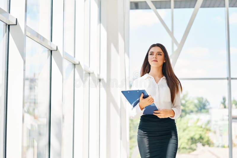 Confident businesswoman going to work holding clipboard in modern office