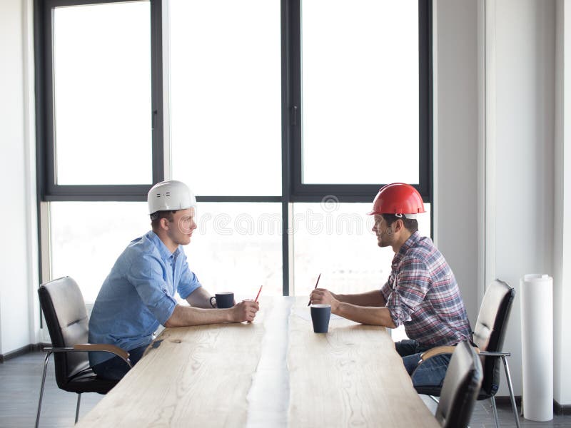 Confident constructors are solving problems while sitting at the table stock photo Confident constructors are solving problems while sitting at the table stock photo