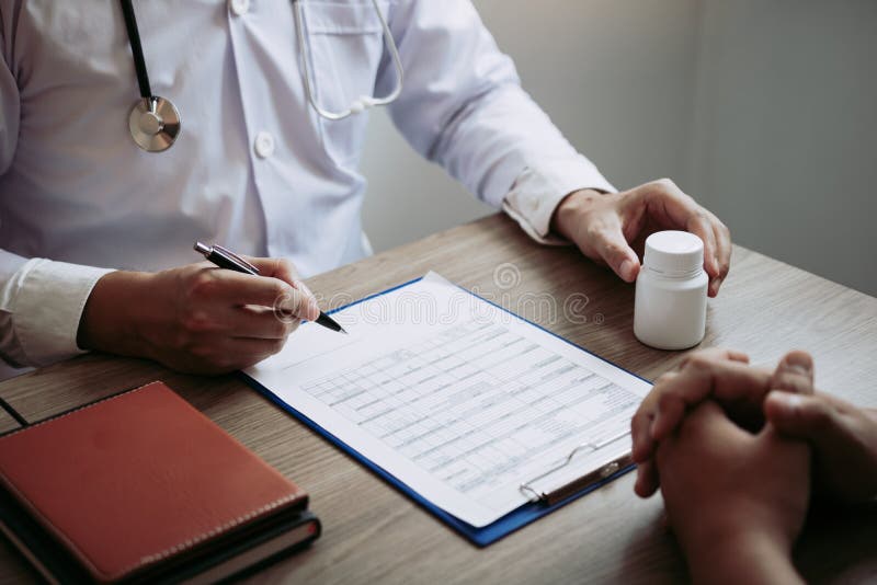 Confident doctor man holding a pill bottle and writing while talking with senior patient and reviewing his medication at office