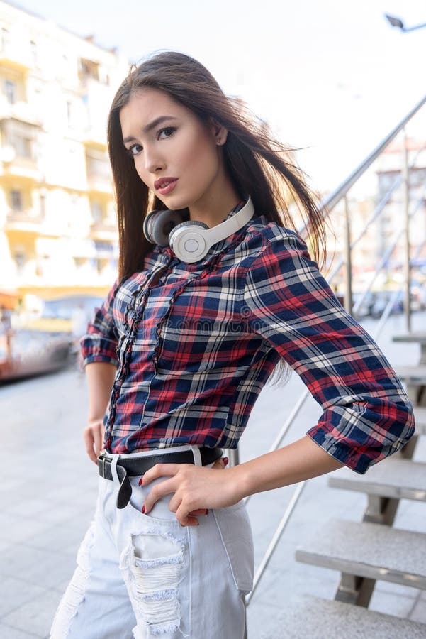 Beautiful young woman is standing with arms akimbo and posing on street. She is looking at camera with confidence. Beautiful young woman is standing with arms akimbo and posing on street. She is looking at camera with confidence