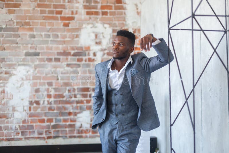 Confident handsome african man in grey three piece suit posing next to a metal structure in the loft style studio