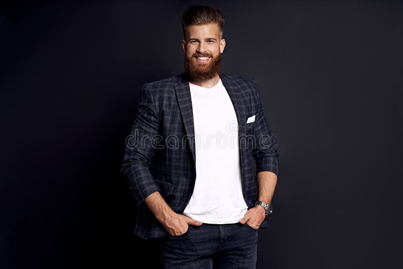 Confident and handsome. Young man with ginger beard in smart-casual clothes smiling looking at camera while posing against black
