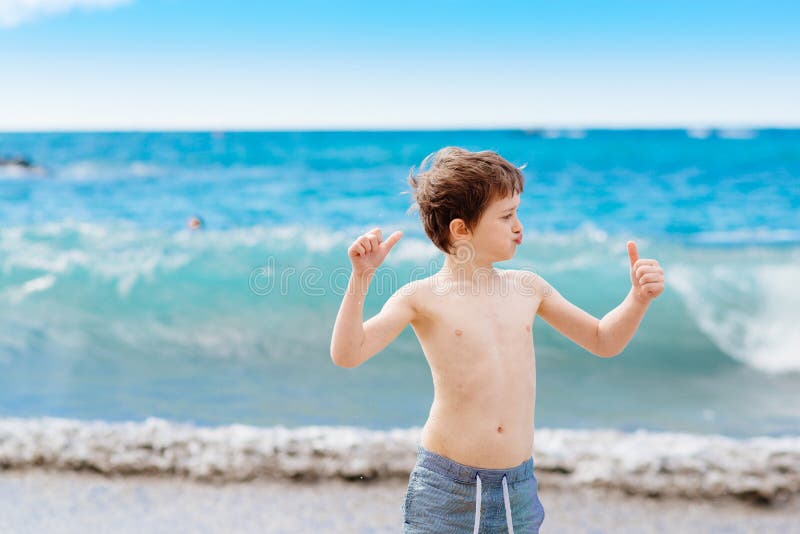 Confident little boy showing his muscles while playing at the beach