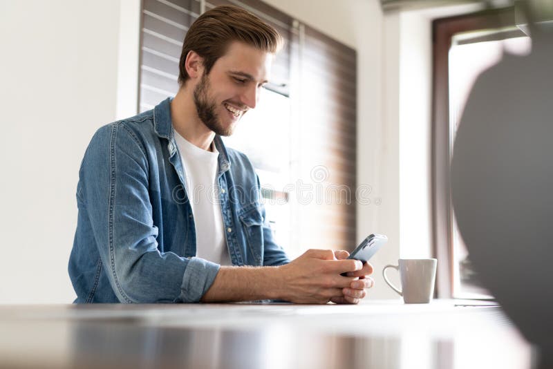 Confident man holding smartphone, sitting in kitchen, chatting online with friends or colleagues, browsing app royalty free stock photos Confident man holding smartphone, sitting in kitchen, chatting online with friends or colleagues, browsing app royalty free stock photos