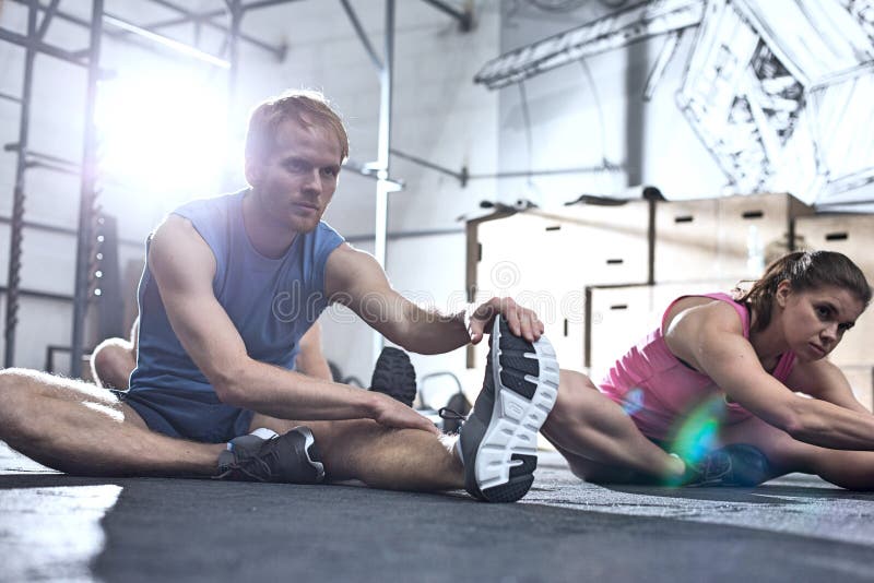 Confident man and woman doing stretching exercise in crossfit gym