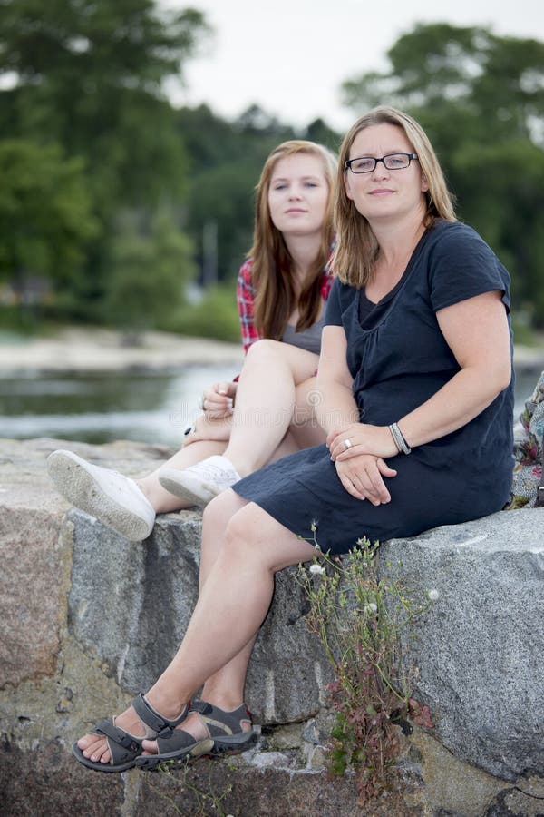 Mother and teenage daughter sitting together outdoors with a safe, happy expression. Mother and teenage daughter sitting together outdoors with a safe, happy expression.