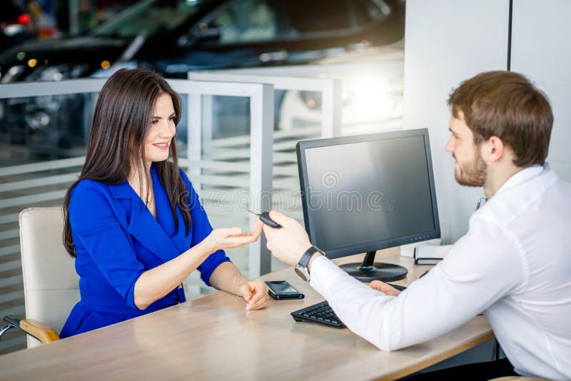 Confident salesman handing over car keys to a female customer completing profitable deal. Confident salesman handing over car keys to a female customer completing profitable deal