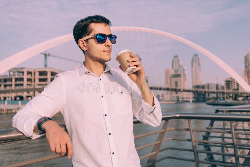 Successful male businessman drinks coffee on the Dubai Creek Canal embankment with the beautiful Tolerance royalty free stock images