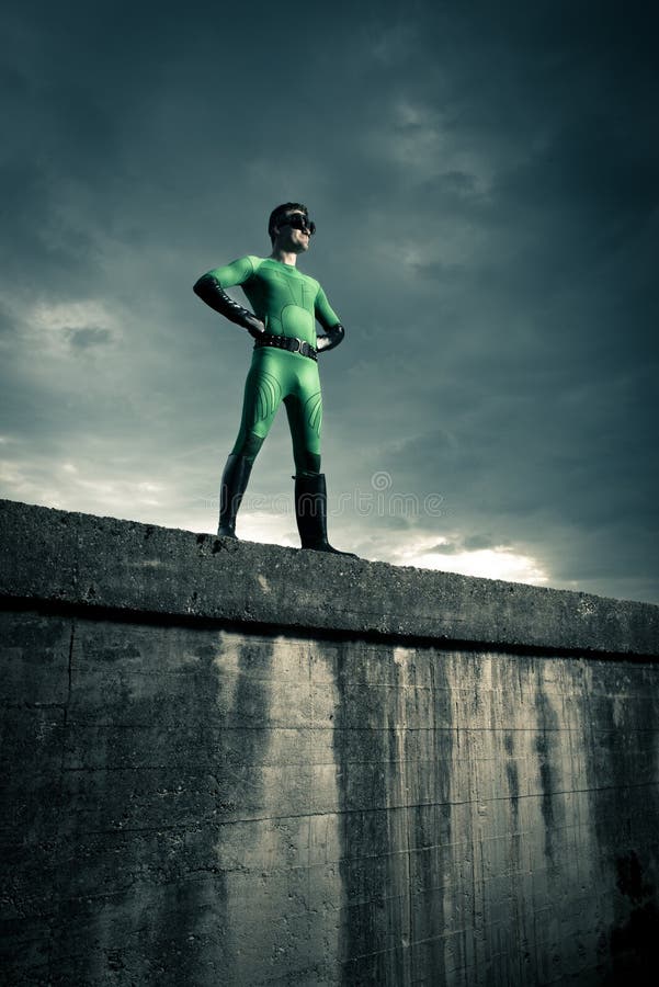 Green confident superhero standing against a cloudy sky with arms akimbo. Green confident superhero standing against a cloudy sky with arms akimbo.