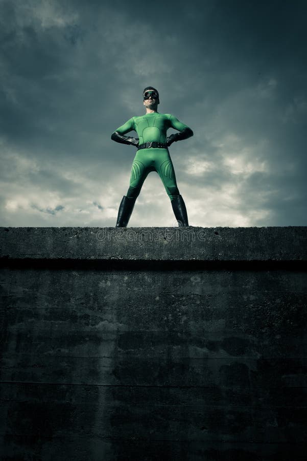 Green confident superhero standing against a cloudy sky with arms akimbo. Green confident superhero standing against a cloudy sky with arms akimbo.