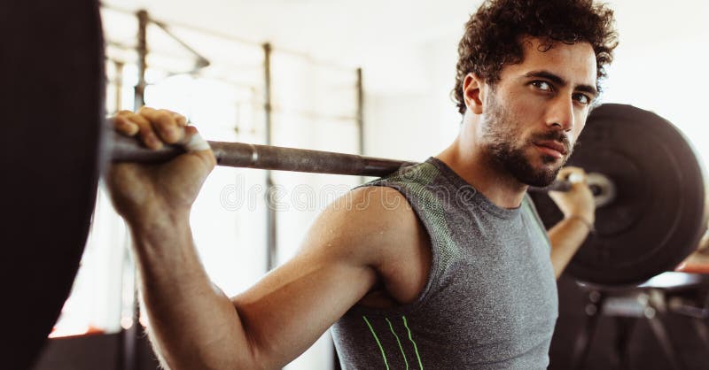 Confident young man exercising with barbell. at fitness center. Male bodybuilder working out with heavy weights at cross training gym.