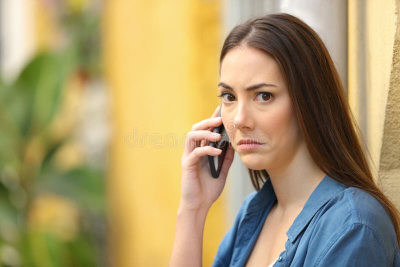 Confused woman looks at you talking on phone in the street