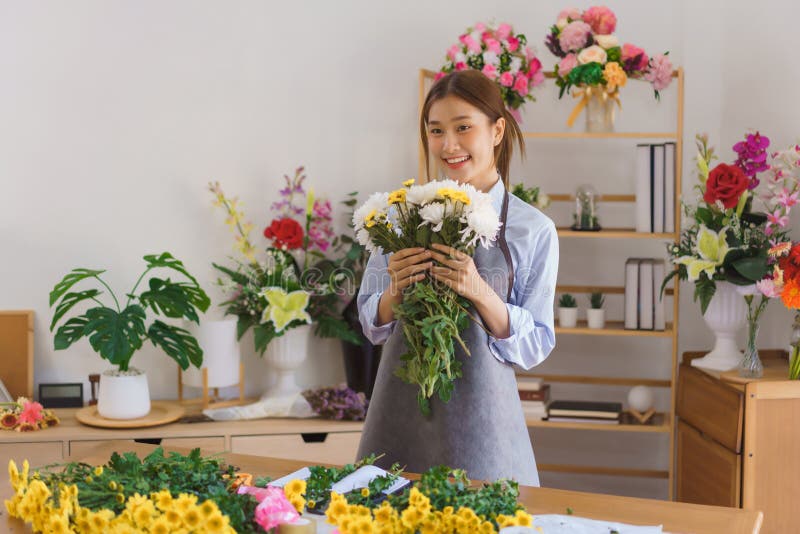 Congettura floristica donna fiorista che sorride e tiene in mano il crisantemo bianco e giallo in un negozio di fiori fotografie stock