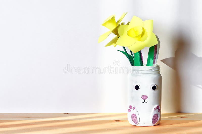 Coniglietto del vaso di DIY Pasqua con il narciso, narcisi dal barattolo di vetro, feltro, occhi sul fondo bianco della parete