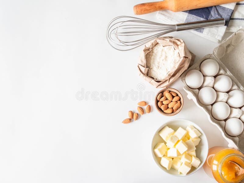 Conjunto de varios ingredientes de cocción harina huevos mantequilla azúcar miel nueces y utensilios de cocina sobre fondo blanco.