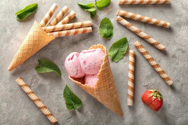 Conos de la galleta con helado y palillos deliciosos de la fresa en fondo gris foto de archivo libre de regalías Conos de la galleta con helado y palillos deliciosos de la fresa en fondo gris foto de archivo libre de regalías