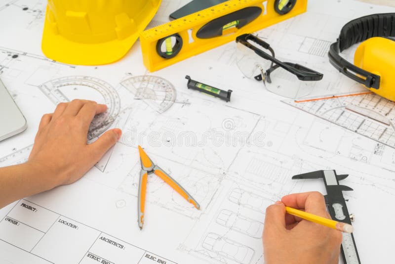 Consegni i piani della costruzione con lo strumento giallo di disegno e del casco fotografia stock Consegni i piani della costruzione con lo strumento giallo di disegno e del casco fotografia stock