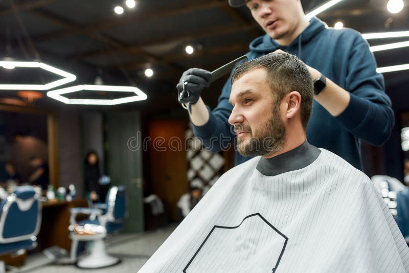 Conseguir Un Nuevo Corte De Pelo. Hombre Apuesto Sentado En Un Sillón En La  Barbería Mientras Barbero Profesional Con Tijeras Y Pe Foto de archivo -  Imagen de piel, estilista: 187357966