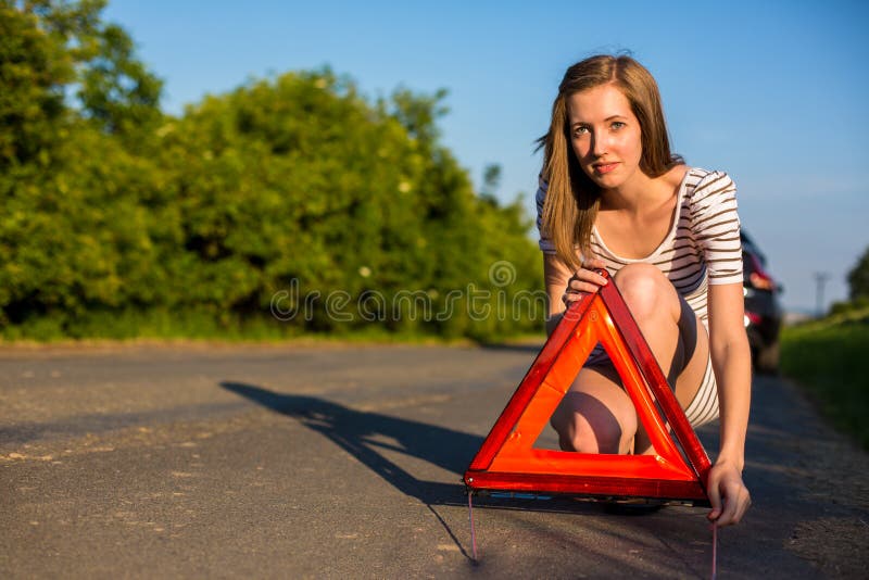 Consideravelmente, jovem mulher que ajusta o triângulo da segurança na borda da estrada fotos de stock Consideravelmente, jovem mulher que ajusta o triângulo da segurança na borda da estrada fotos de stock