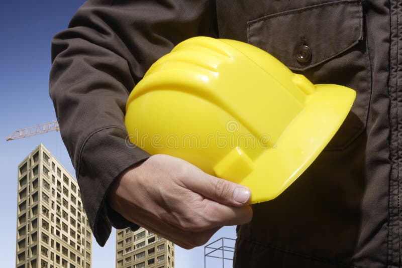 Construction worker holding yellow hardhat with building background. Architect uniform stock images, royalty-free photos and pictures