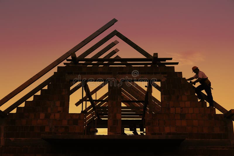 Construction worker working with house wooden roof against sunset sky. Construction worker working with house wooden roof against sunset sky