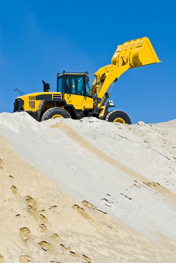 Giallo macchine per la costruzione di front-end loader sulla sommità di un cumulo di sabbia contro un cielo blu.