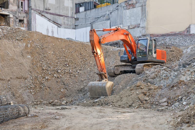 Horizontal photo of a construction site. There is an orange excavator loading machine. This is the foundation of a building. Everything is muddy and candid in the picture.