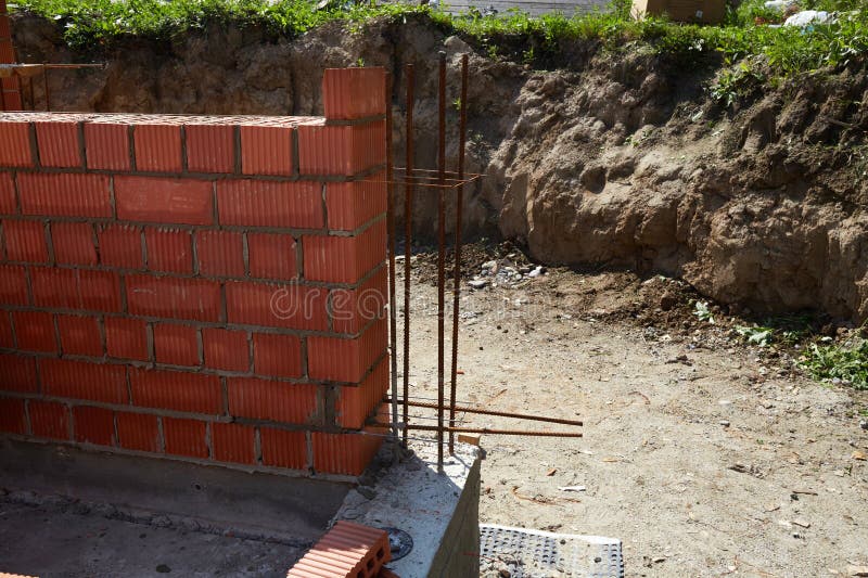 A construction site features a newly built brick wall with visible rebar bars extending from the concrete foundation stock image