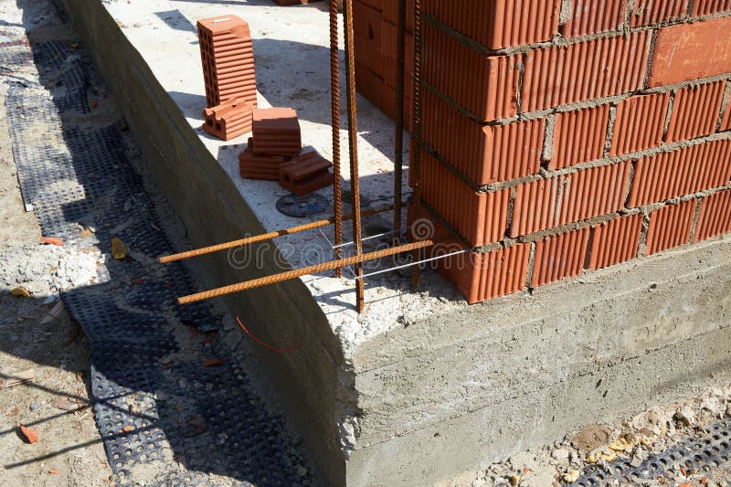 A construction site features a newly built brick wall with visible rebar bars extending from the concrete foundation. royalty free stock images