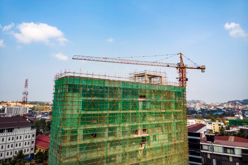 Construction site next to modern office, residential building. Working crane and safety net with cloud blue sky . Green grid prevent objects falling from height. Industrial background. Construction site next to modern office, residential building. Working crane and safety net with cloud blue sky . Green grid prevent objects falling from height. Industrial background