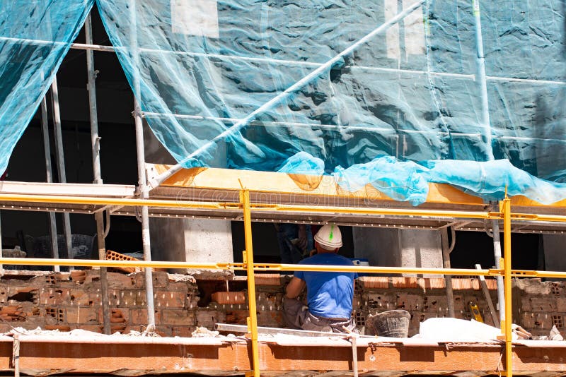 Construction site of old apartment building with scaffolding and a busy mason worker. Bricklayer bricking a new row of bricks on