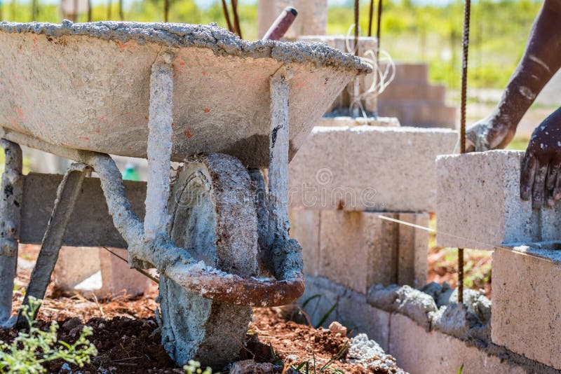 Construction site. Wheelbarrow next to mason laying concrete bloc stock photography Construction site. Wheelbarrow next to mason laying concrete bloc stock photography