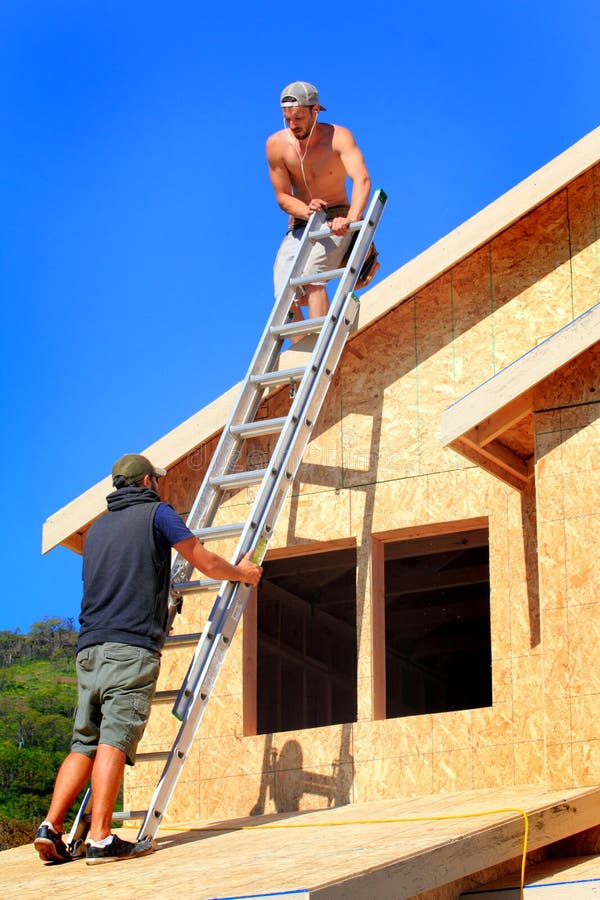 Due di lavoro di uomini che lavorano insieme con una scaletta sulla cima di una casa che è in costruzione.